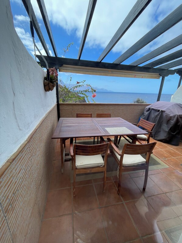 Une terrasse extérieure avec une table et des chaises en bois, une pergola et une vue sur la mer.