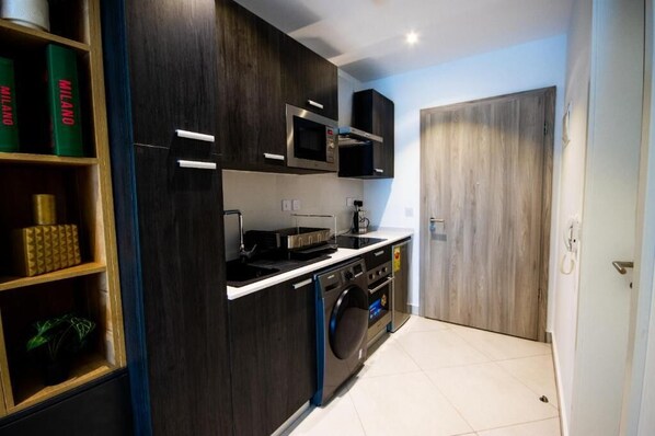 A compact kitchen with dark wood cabinets, a built-in microwave, a washing machine, and a small countertop. - Splendid Apartment at The Lennox (Accra)