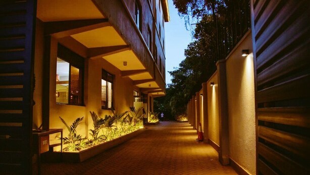 Un pasillo con piso de ladrillo, una jardinera con plantas y un edificio con una persiana cerrada a la derecha.