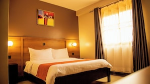 Una habitación de hotel con una cama grande, dos mesitas de noche, un cabecero, un cuadro en la pared y una ventana con cortinas.