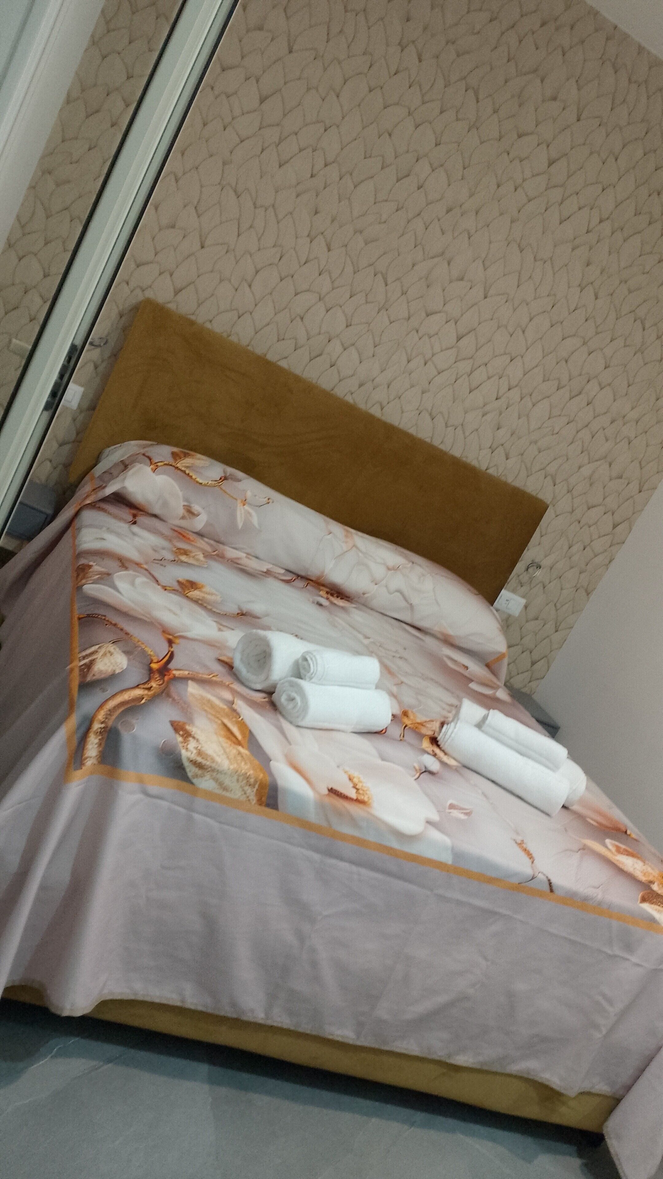 A bed with a patterned bedspread, rolled towels, and a brown headboard.