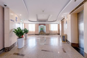A hotel lobby with a reception desk, potted plants, a large mirror, and an elevator. - Xing Yue Hotel (Dongguan Changping Baihua Times Plaza) (Dongguan)