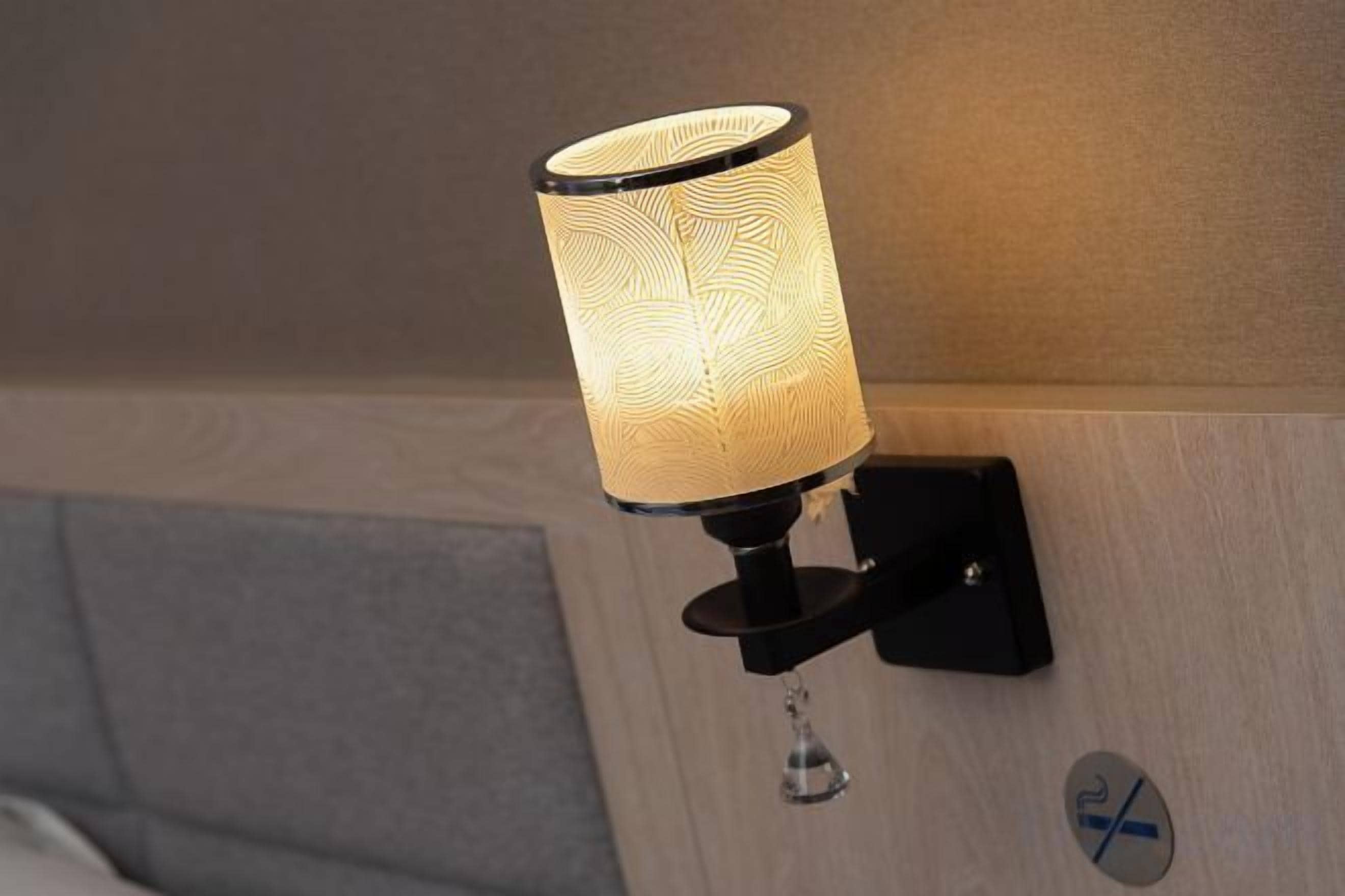 A wall-mounted lamp with a textured shade, a black base, and a clear droplet-shaped light fixture.
