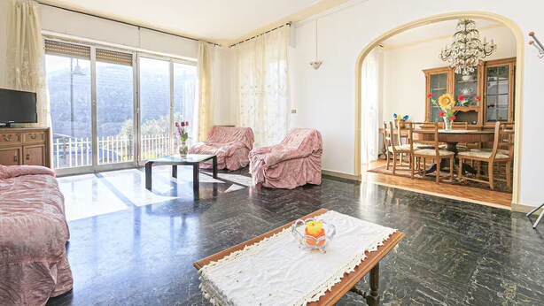 A spacious living room with a large window, a dining area with wooden furniture, and a cozy seating area with covered chairs. - Detached villa with pool and garden in the Ligurian countryside (Gattorna)