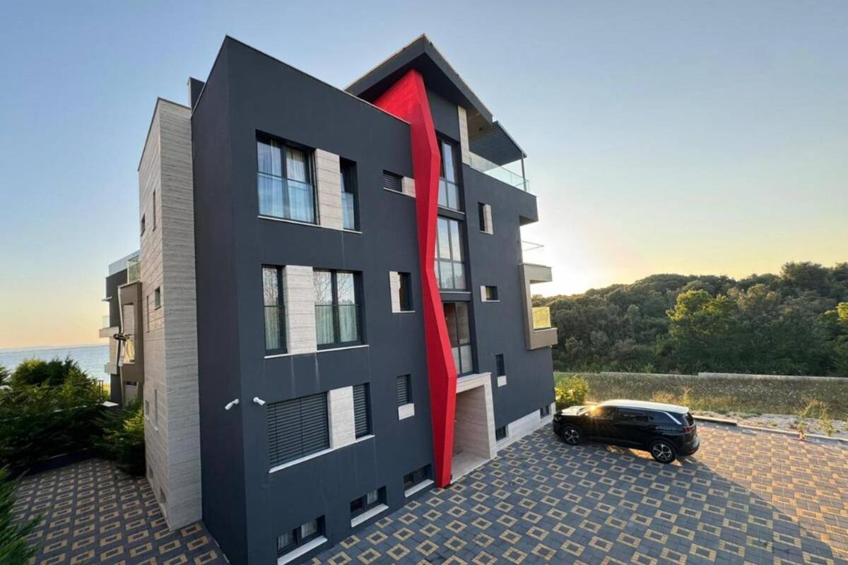 A modern building with a unique red accent, large windows, and a parking area with a car.