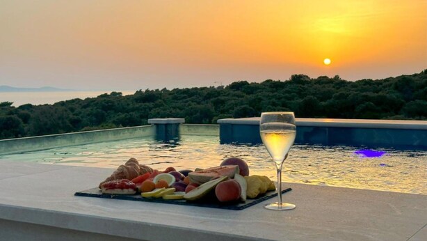 A sunset view from a poolside area with a glass of champagne and a fruit platter. - Leonarda Waterfront Residences (Zadar)