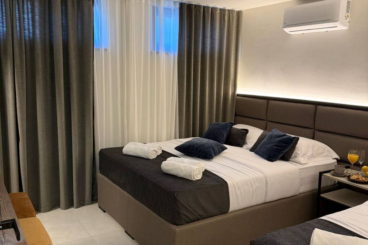 A hotel room with a large bed, a bedside table with a cup and glasses, and a wall-mounted air conditioner.