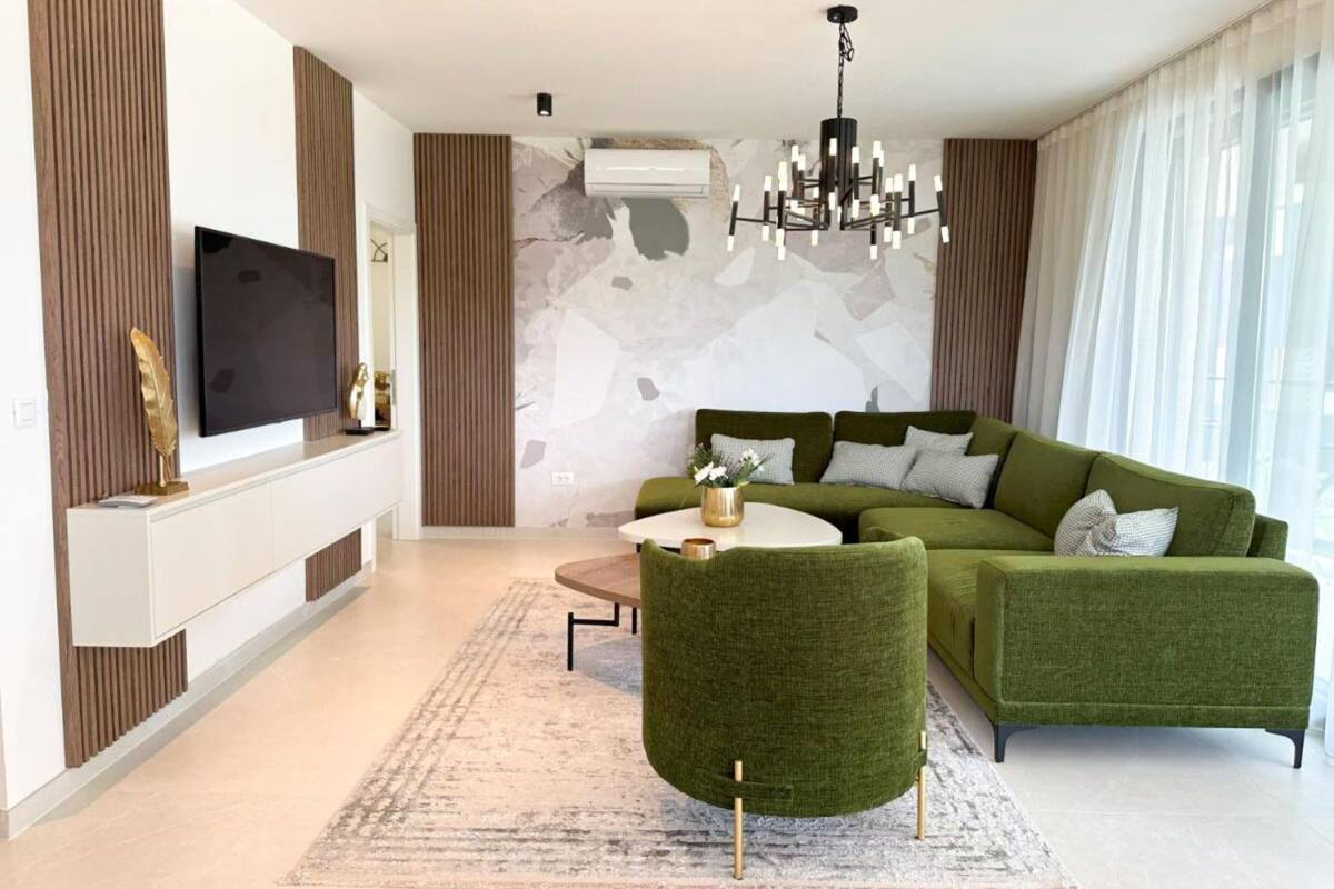 A modern living room with a green sofa set, a round coffee table, and a flat-screen TV mounted on a white console.