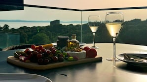 A table with a cheese board, grapes, and a bottle of olive oil, with two glasses of white wine and a scenic view in the background. - Leonarda Waterfront Residences (Zadar)
