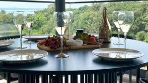 A table with a cheese board, grapes, and a bottle of wine, set against a scenic view. - Leonarda Waterfront Residences (Zadar)