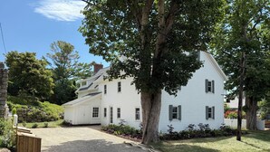 A white two-story house with a gravel driveway and a wooden bench.