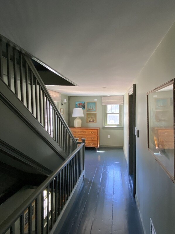 A hallway with a wooden staircase on the left, a wooden dresser in the center, and a door on the right.