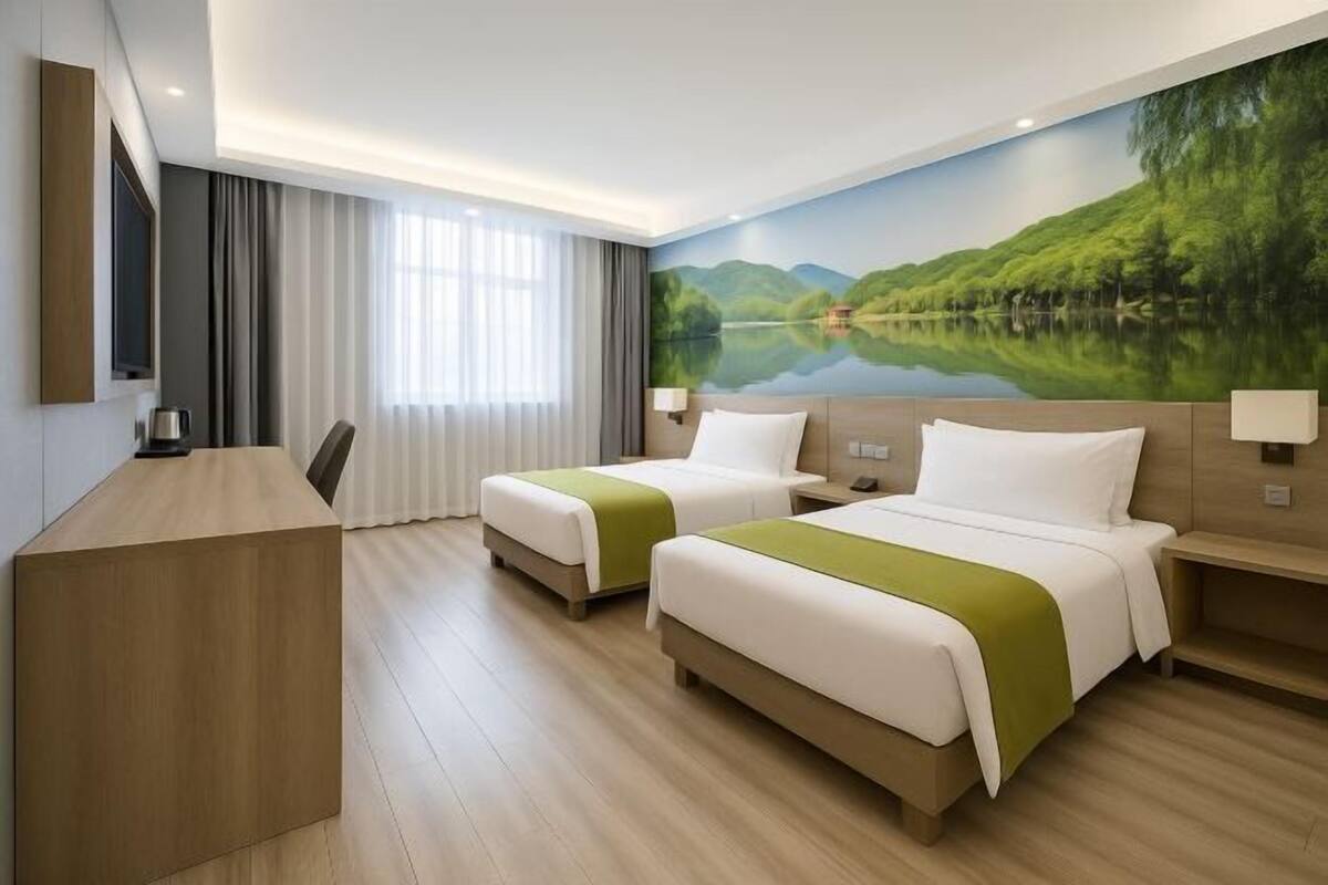 Ein Hotelzimmer mit zwei Betten, einem Schreibtisch und einem großen Wandbild mit See und Bergen.