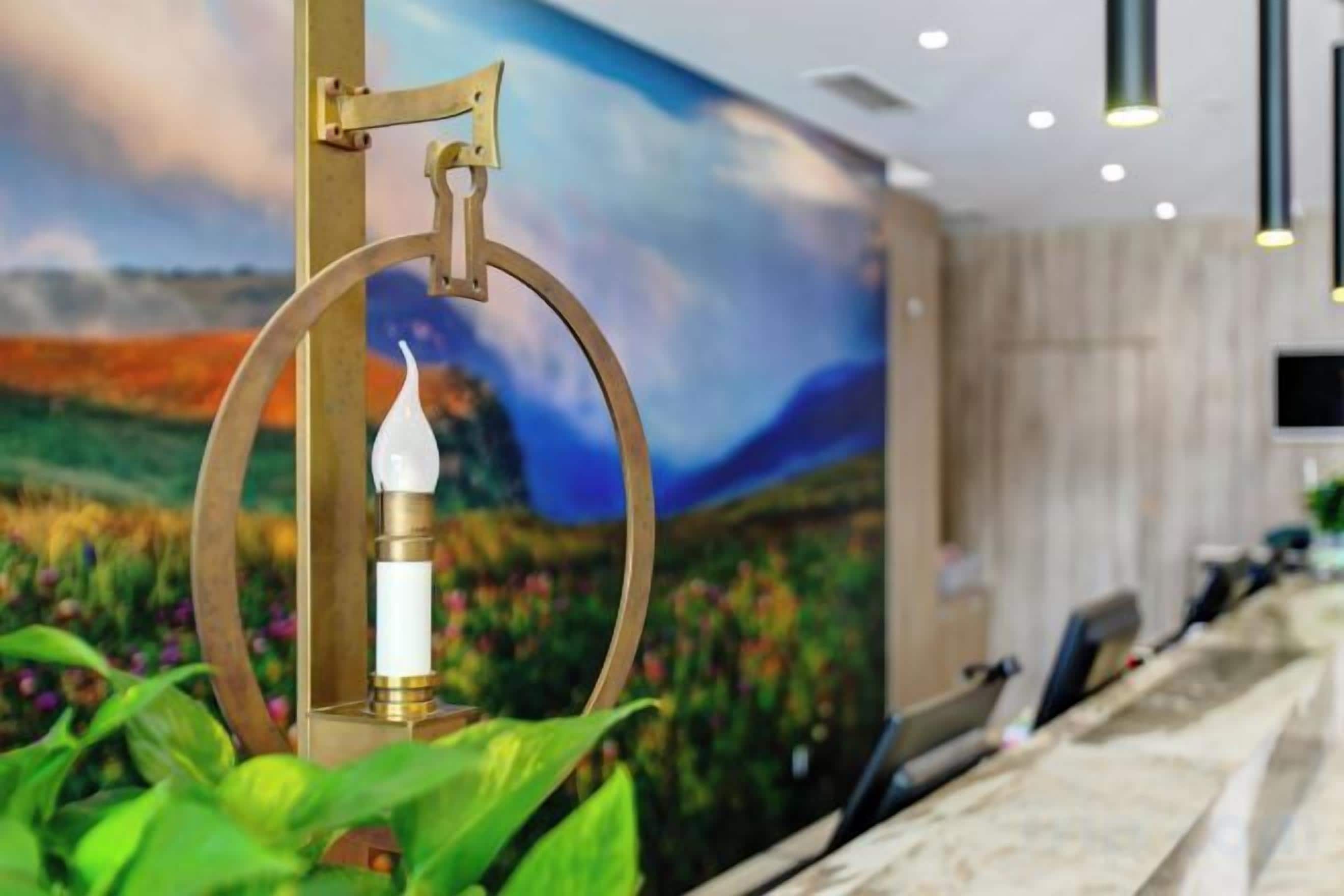 Una vela en un soporte decorativo, un mural con un paisaje y un área de recepción con mostrador y sillas.