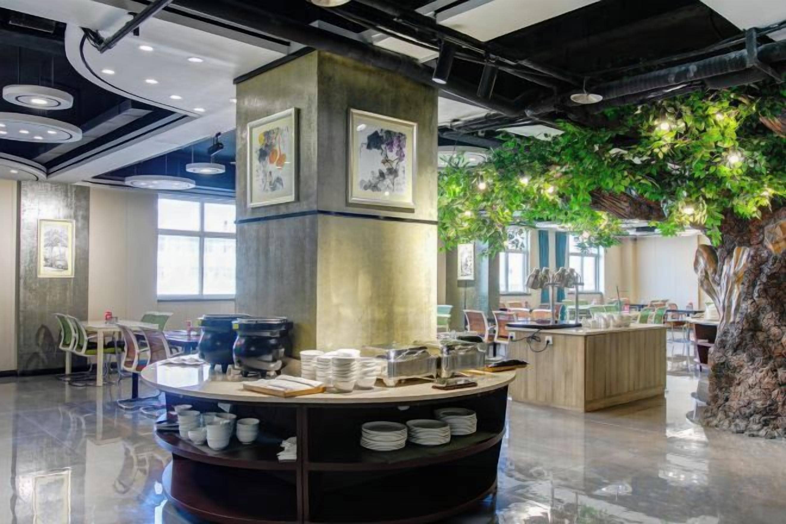 Una cafetería moderna con mostrador central, zona de mesas y una gran decoración de árbol.