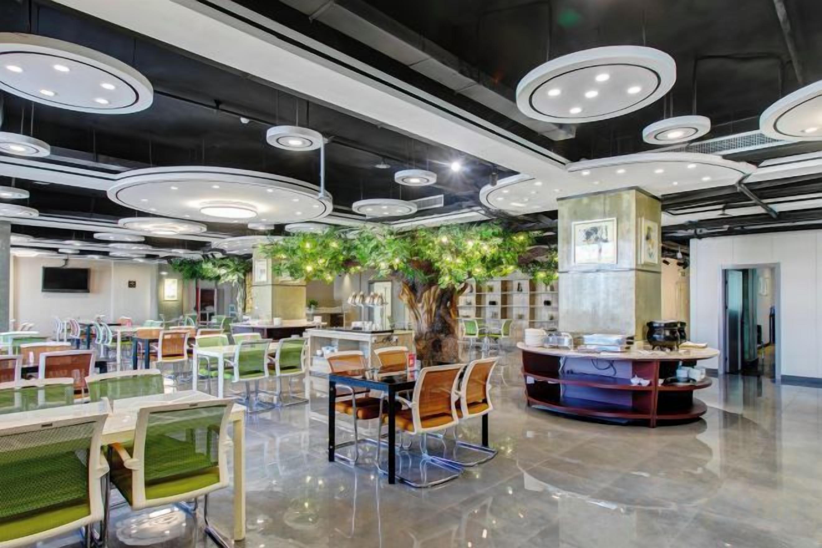 Un moderno vestíbulo de hotel con varias zonas de estar, una planta central y un mostrador de recepción.