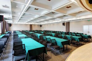 A conference room with rows of tables and chairs, a stage, and a white ceiling with recessed lighting. - Yuncheng Juhetai Hotel (Yanhu South Wind Square) (Yuncheng)