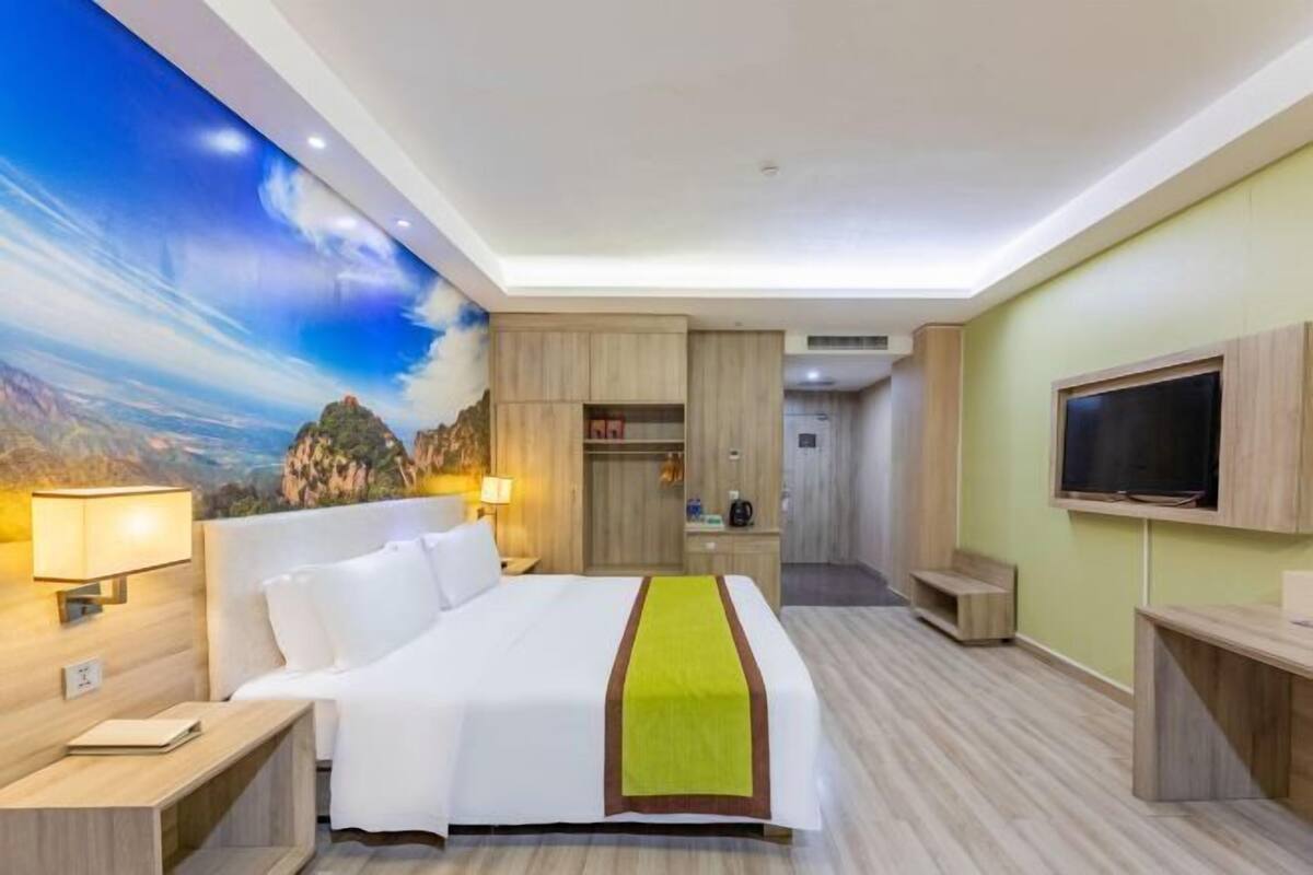 Ein Hotelzimmer mit Bett, Fernseher, Schreibtisch, Kleiderschrank und Wandgemälde.