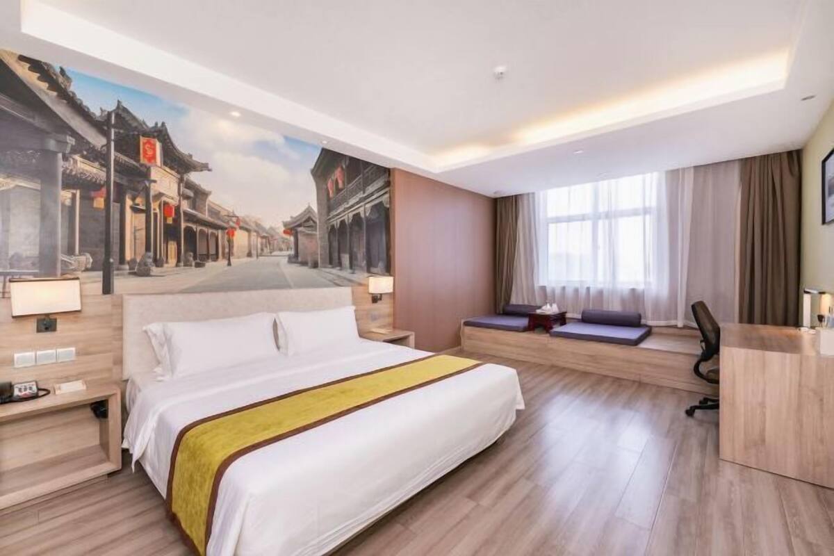 Ein Hotelzimmer mit einem großen Bett, einem Schreibtisch, einer Bank und einem Wandgemälde einer Straßenszene.