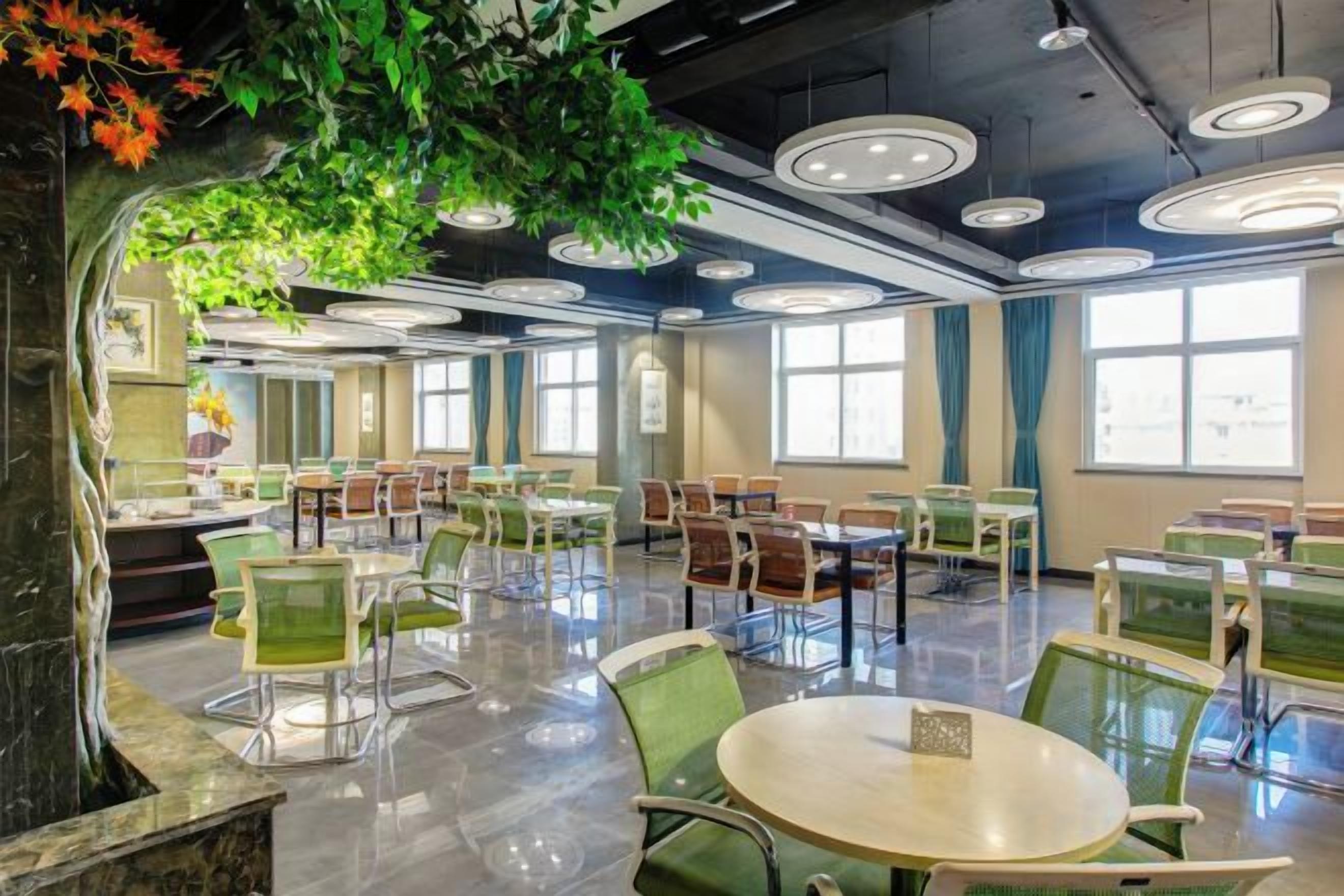 A spacious indoor dining area with round tables and chairs, large windows, and a ceiling with circular light fixtures.