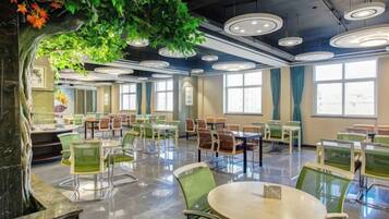 A spacious indoor dining area with round tables and chairs, large windows, and a ceiling with circular light fixtures.