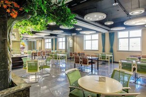 Un comedor amplio con mesas y sillas redondas, ventanas grandes y un techo con luminarias circulares.