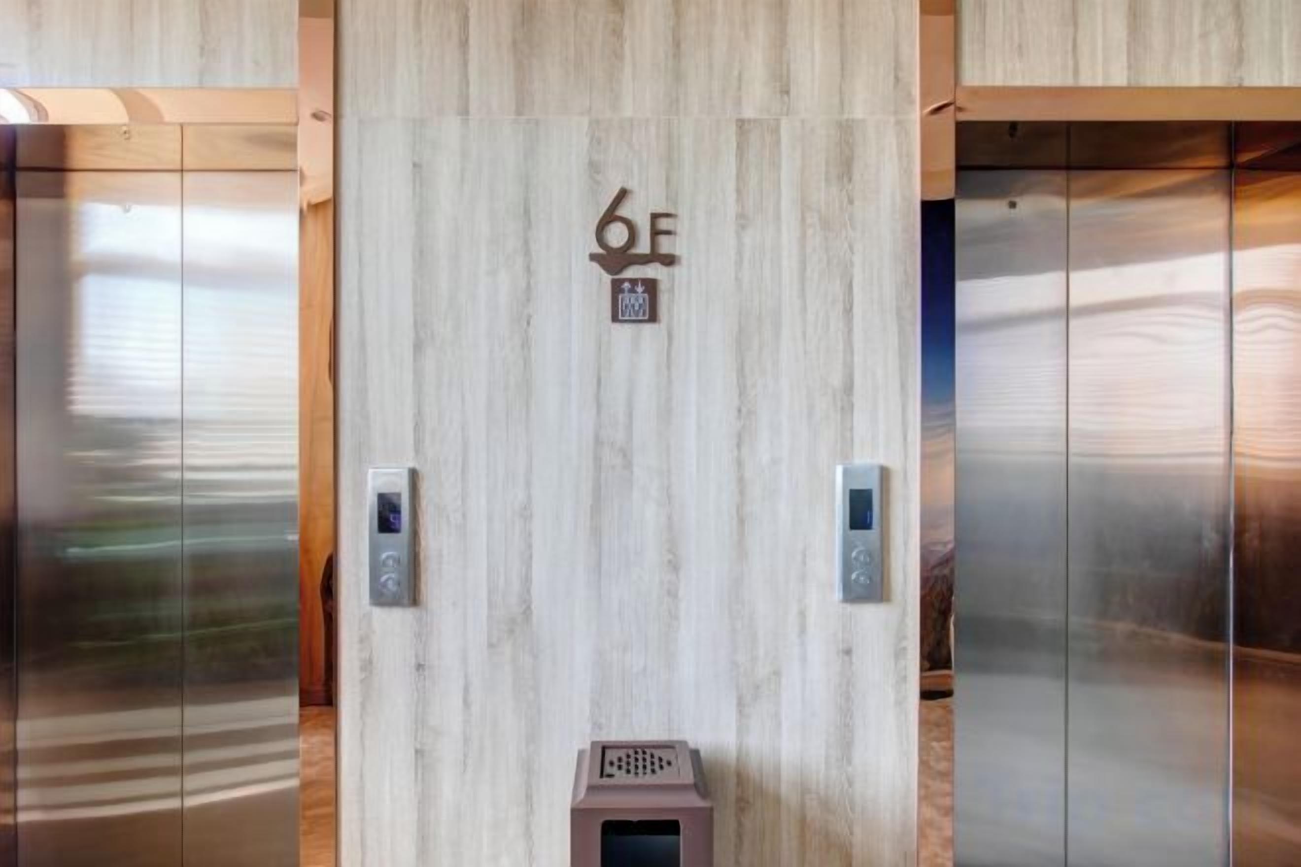 L’intérieur d’un ascenseur, avec un mur revêtu de panneaux en bois, un écran numérique et une porte d’ascenseur métallique.