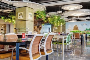 Un interior de restaurante moderno con mesas redondas, sillas y un árbol decorativo en el centro.