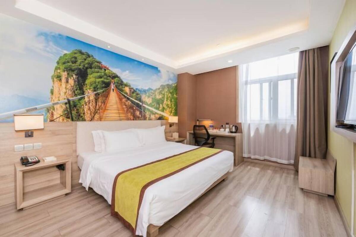 Ein Hotelzimmer mit Bett, Schreibtisch, Stuhl und einer großen Wandmalerei einer Brücke.