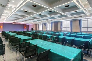 A conference room with rows of tables and chairs, large windows, and a high ceiling with lighting fixtures.