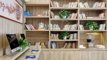 A wooden bookshelf with books and plants, a desk with a computer and a plant, and a framed picture on the wall.