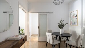 Ein moderner Essbereich mit einem runden Tisch, vier Stühlen, einer hölzernen Bank, einer Topfpflanze und einem gerahmten Kunstwerk an der Wand.