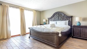 Un dormitorio con una cama grande, dos mesitas de noche con lámparas y vistas a través de una ventana con cortinas.