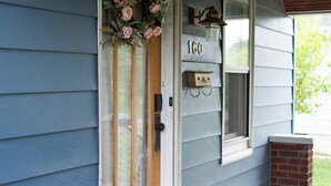 A house with a blue exterior, a wooden door with a glass panel, a number '160' above the door, and a small brick structure to the right.