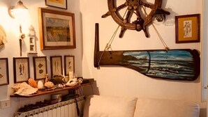 Een gezellige woonkamer met een beige bank, een houten stuurrad en diverse ingekaderde foto’s aan de muur.