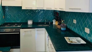 Een keuken met witte kastjes, een zwart fornuis en een groen aanrecht.