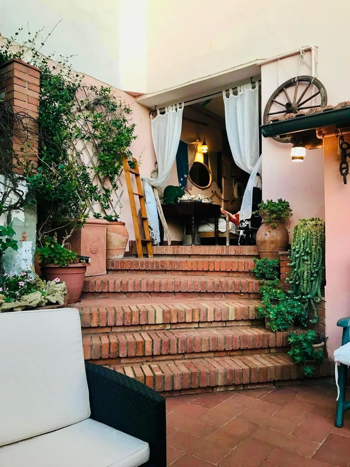 Una escalera de ladrillo conduce a una habitación con una cama, una silla de madera y una planta en maceta.