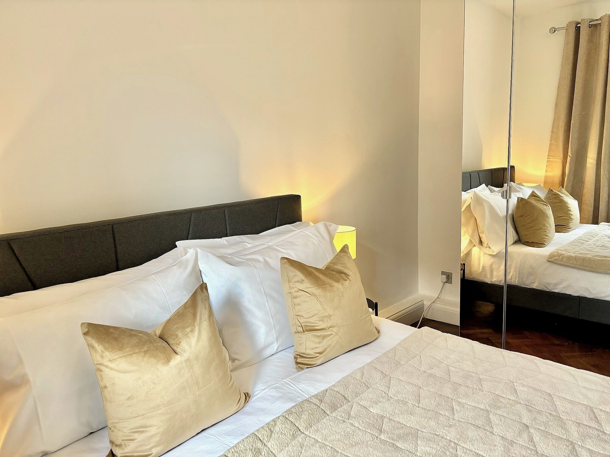 Una cama bien hecha con almohadas blancas y beige, una colcha acolchada y una lámpara de noche.