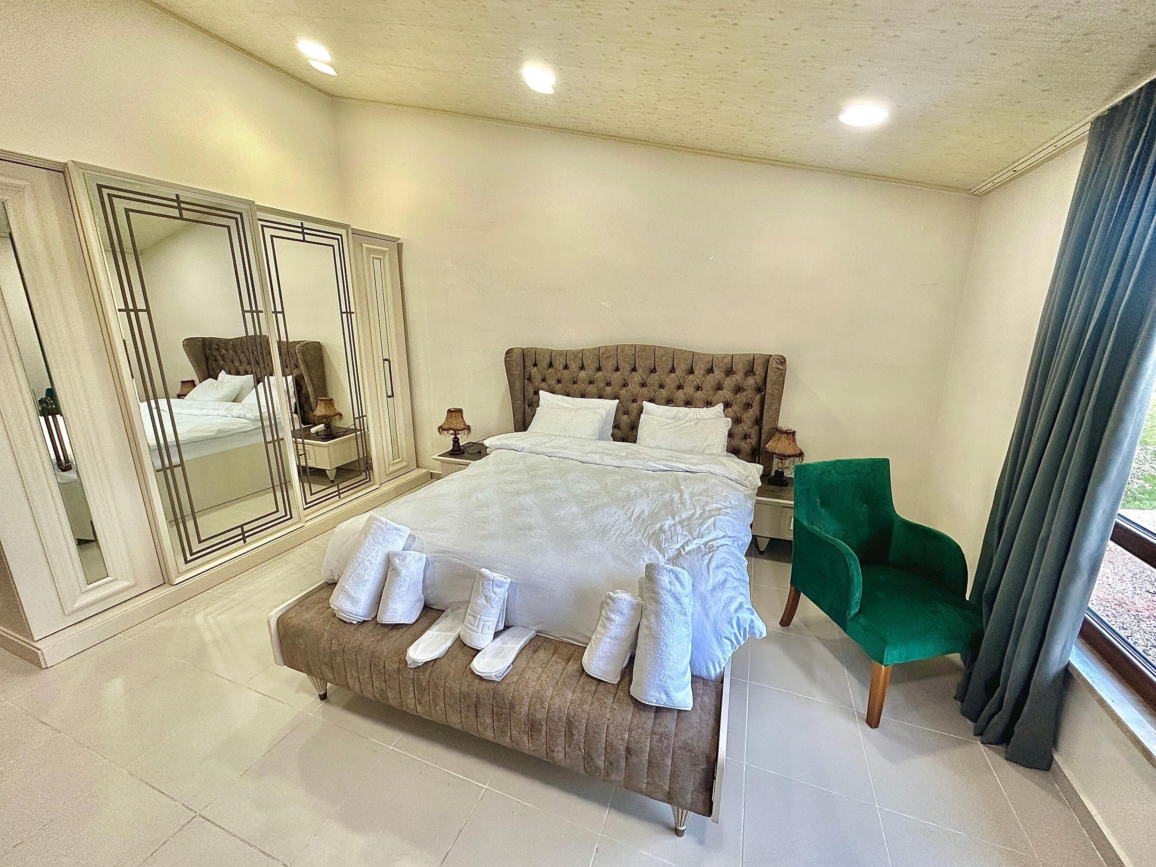 Una habitació espaiosa amb un llit gran, una butaca verda, un mirall i vista a l'exterior.
