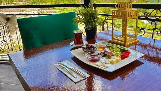 A table set with a meal, a potted plant, and a view of a mountainous landscape. - Kaşkaloğlu Hotel (Arapgir)