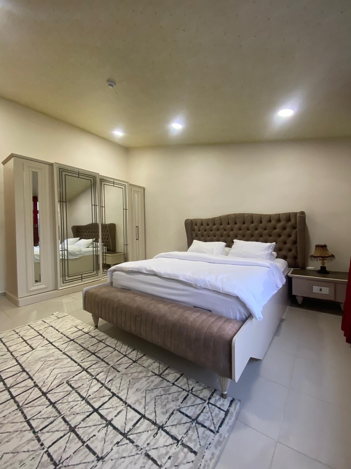 Een slaapkamer met een groot bed, een kledingkast, een spiegel en een nachtkastje.