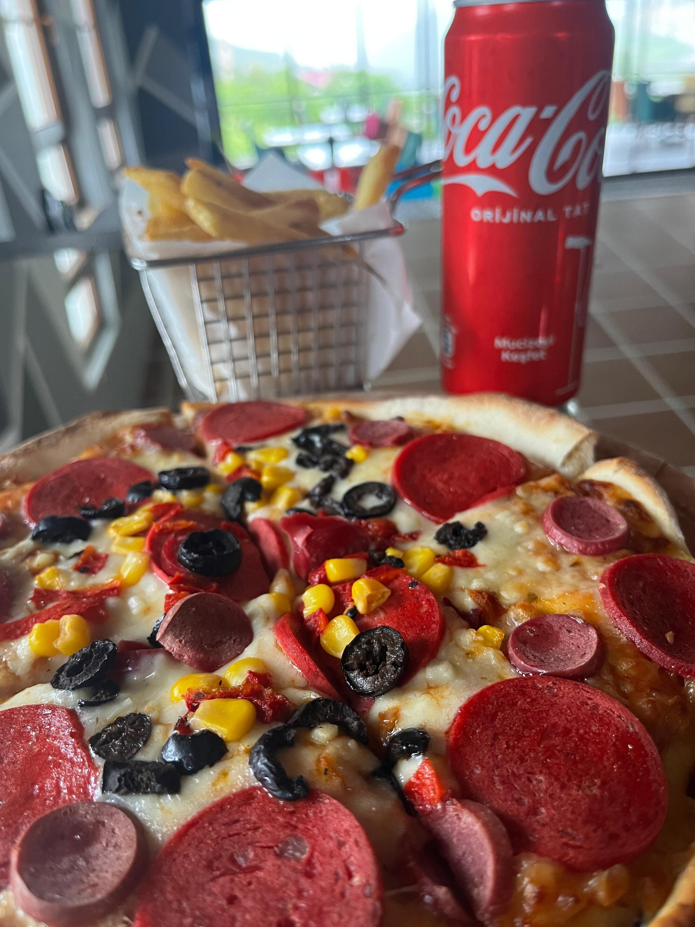A pizza with pepperoni, black olives, and corn, a basket of fries, and a Coca-Cola can.