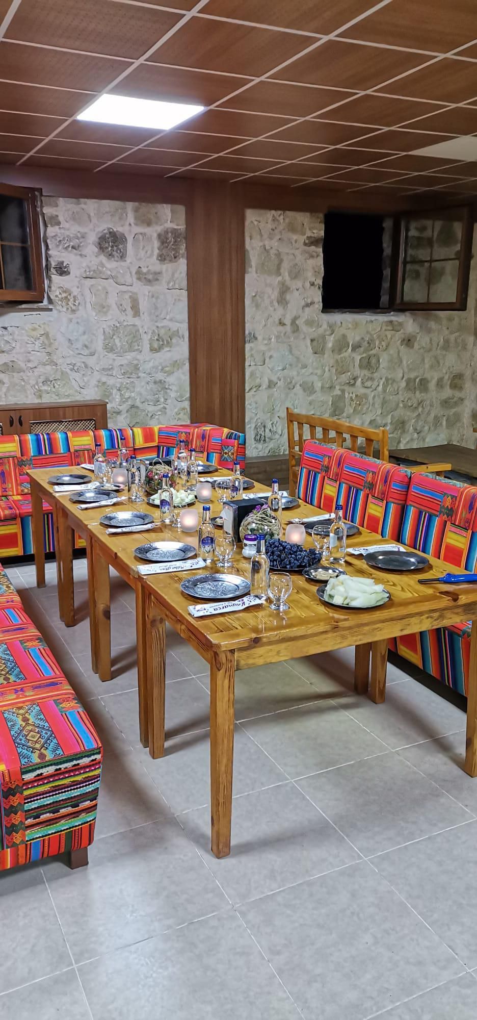 A dining area with a long wooden table set for a meal, surrounded by colorful upholstered benches.