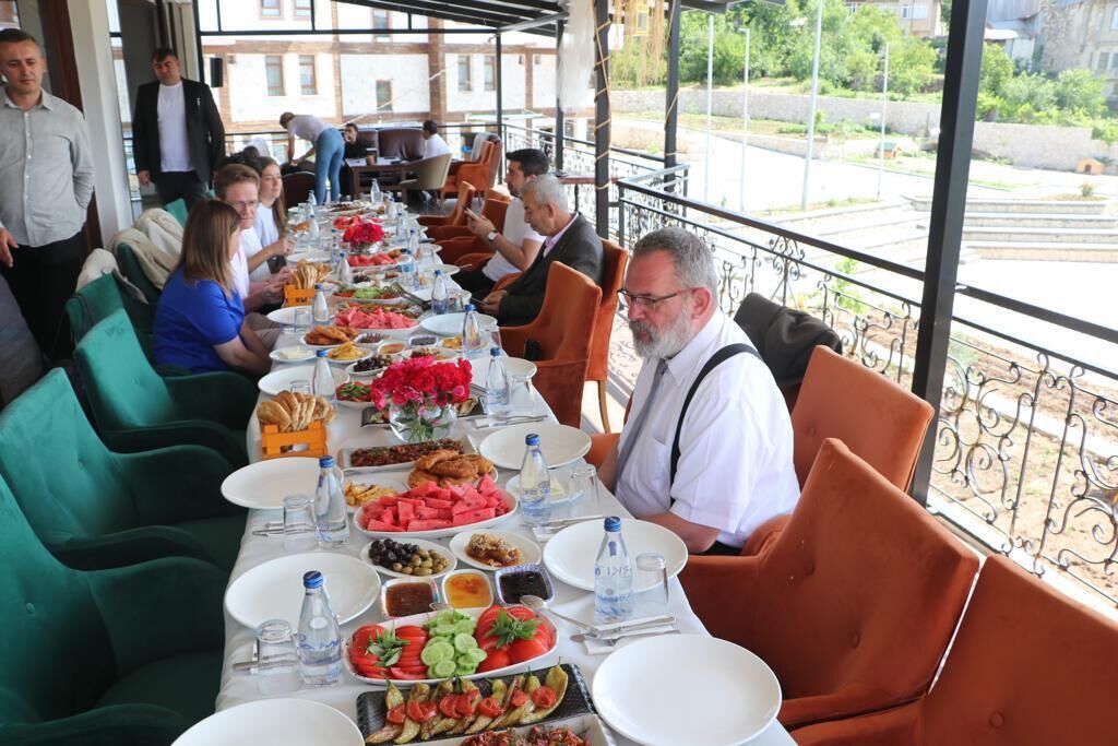 Una larga mesa de comedor con diversos platos y bebidas, rodeada de sillas verdes y anaranjadas.