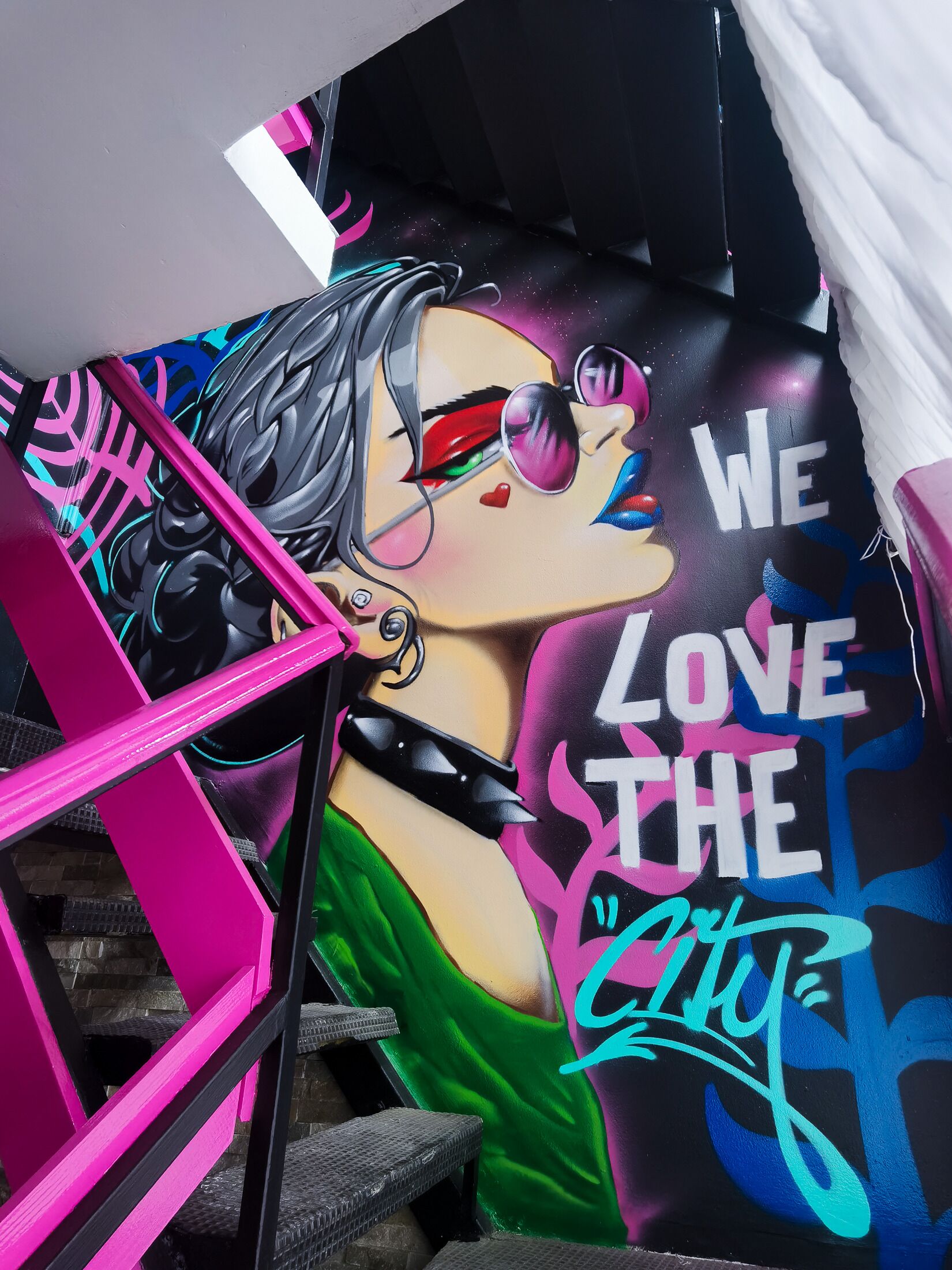 Een trap met een levendige muurschildering van een vrouw en de tekst 'We Love the City'.