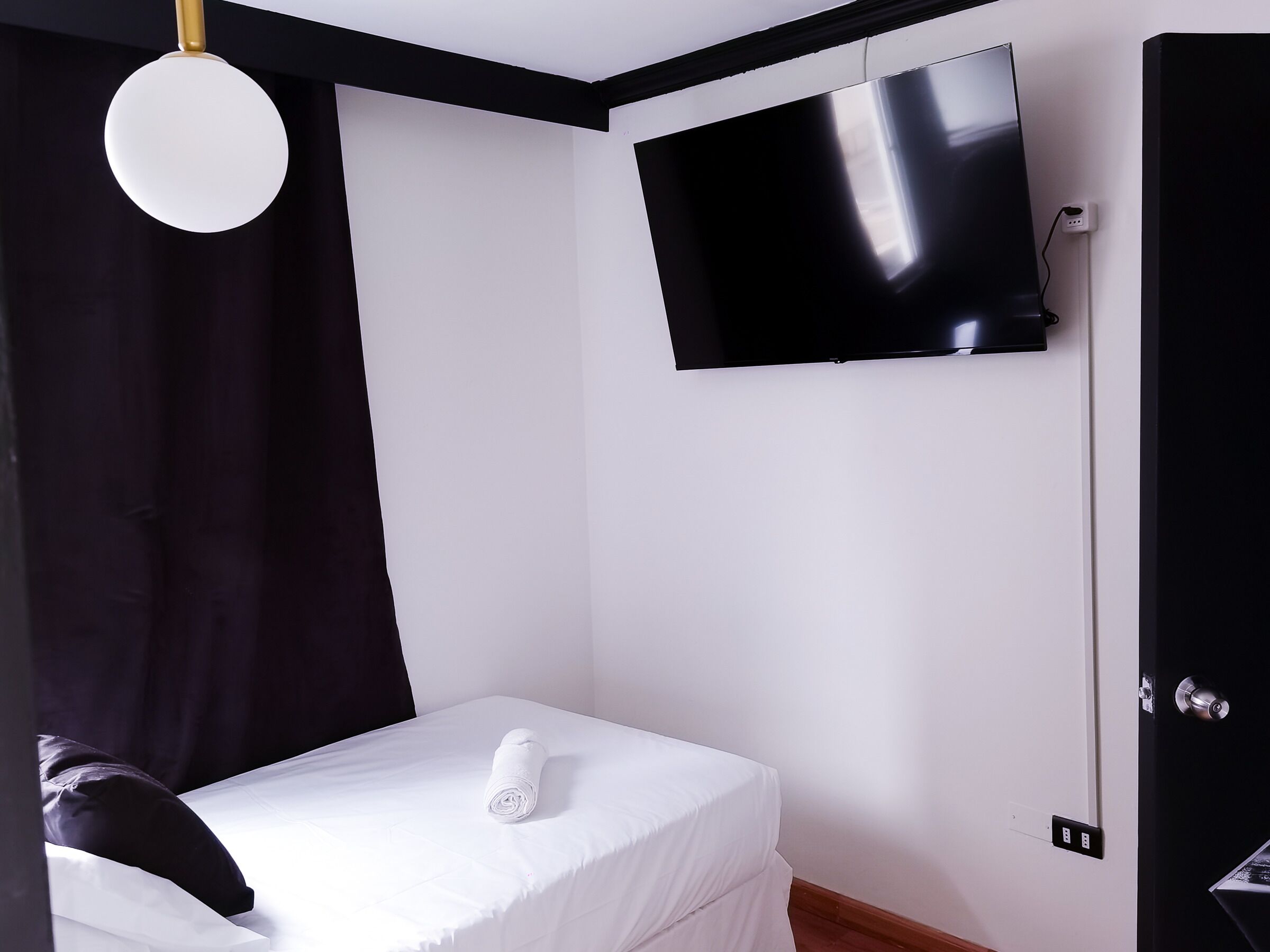 A modern hotel room with a bed, a flat-screen TV mounted on the wall, and a door with a handle.