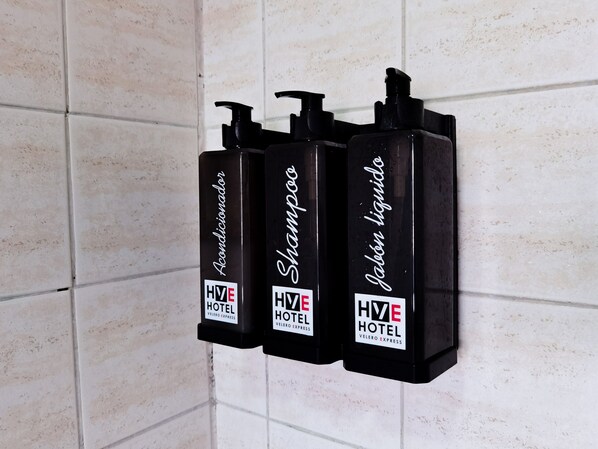 Three black toiletries dispensers labeled 'HVE HOTEL' and 'Velero Express' on a tiled wall. - hotel velero express (Iquique)