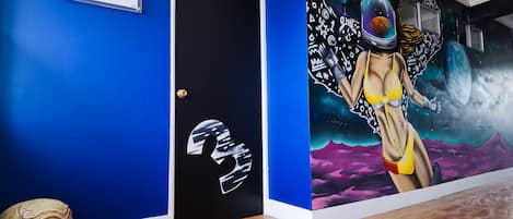 A room with a blue wall, a black door, and a mural of a space-themed figure.