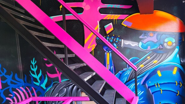 Un escalier avec des rampes roses et une fresque représentant un robot et une femme.