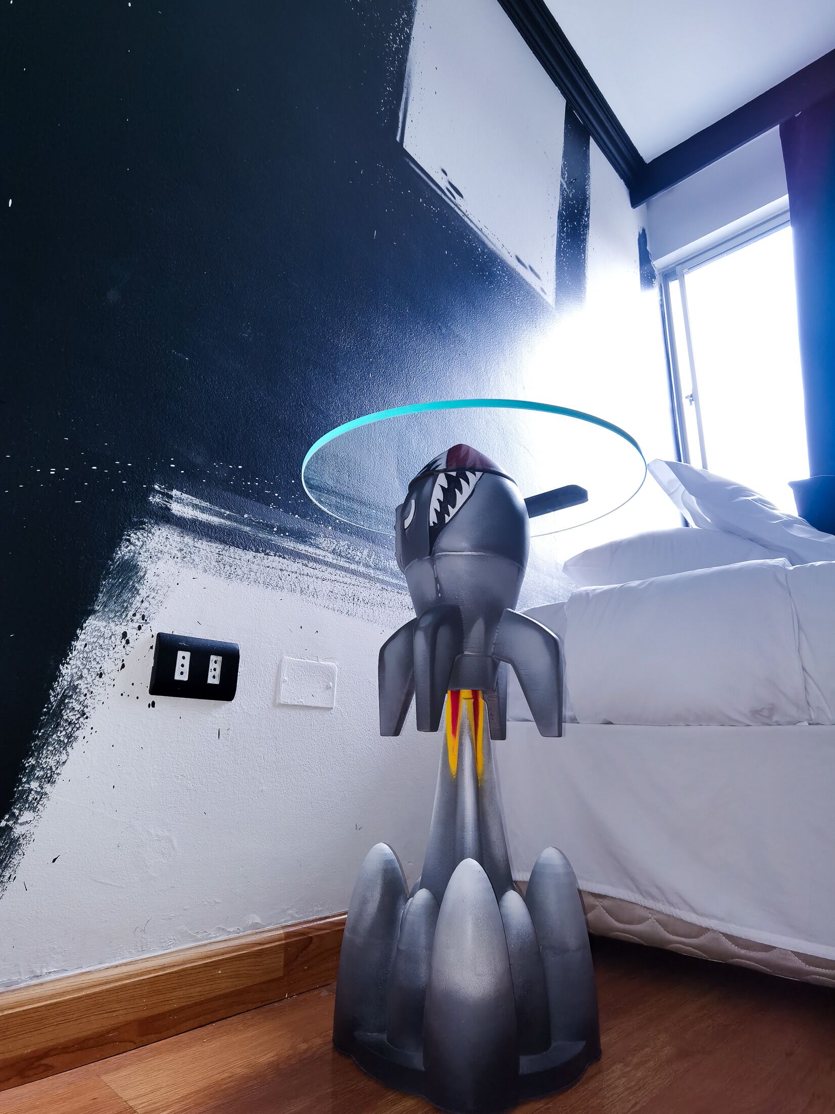 A room with a bed, a window, and a wall with a light switch and electrical outlet.